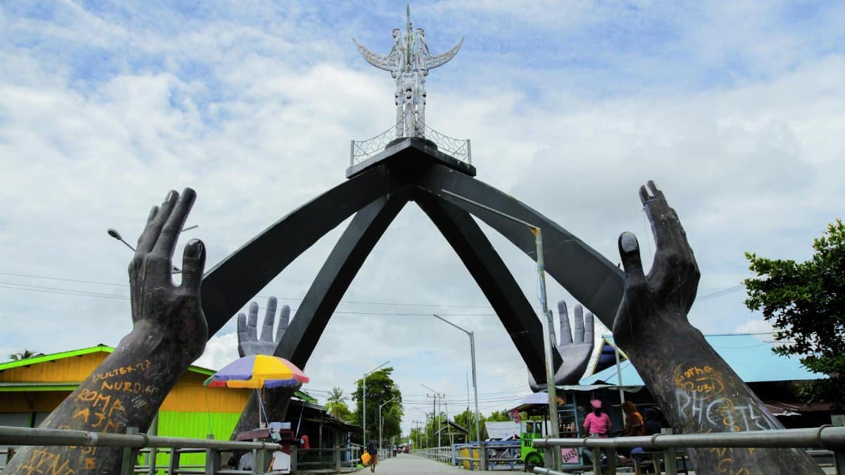 Monument in Agats, Papua with large hands sculpture and urban surroundings.