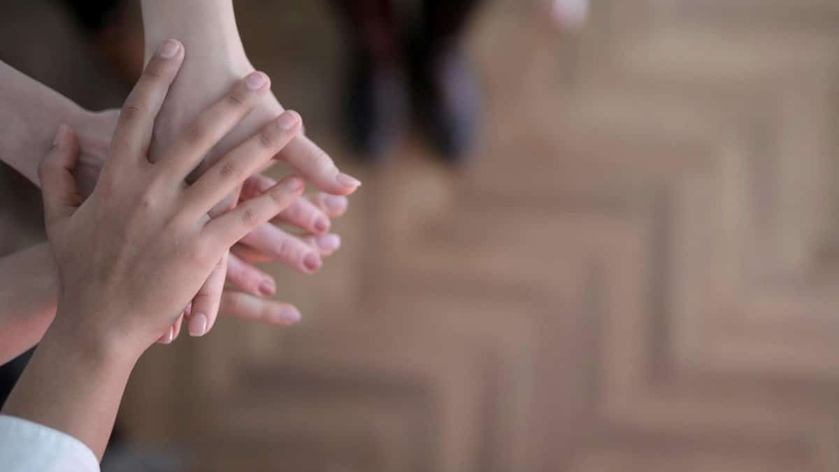 Unrecognizable crop people holding hands together in teamwork and support above wooden brown floor