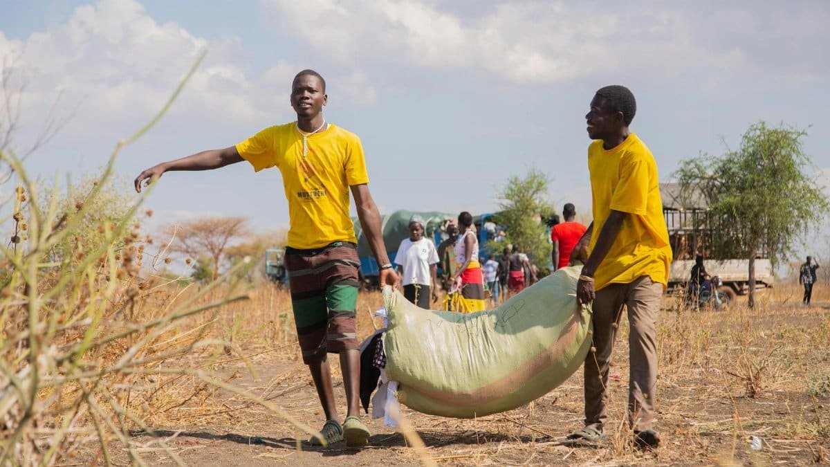 Volunteers in yellow shirts transport aid supplies in a rural landscape, highlighting community assistance.