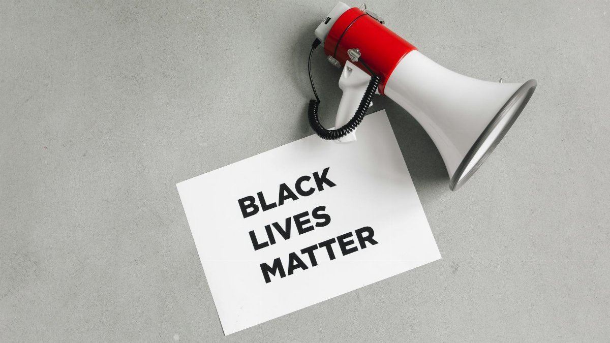 A Black Lives Matter sign placed next to a megaphone on a neutral background.
