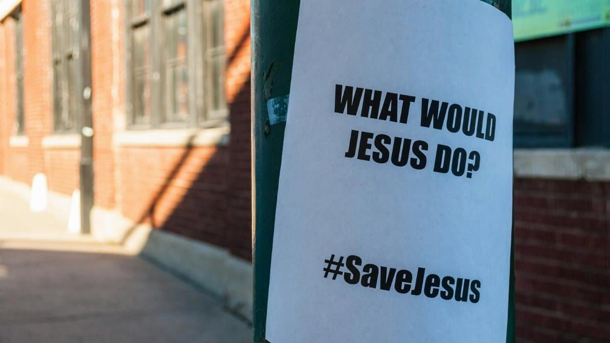 A flyer on a city street pole with the message 'What Would Jesus Do?' and '#SaveJesus'.