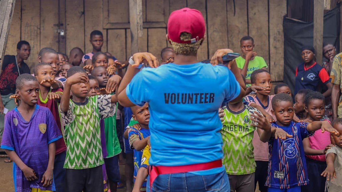 A volunteer guides a diverse group of children in an outdoor activity, fostering community spirit and teamwork.