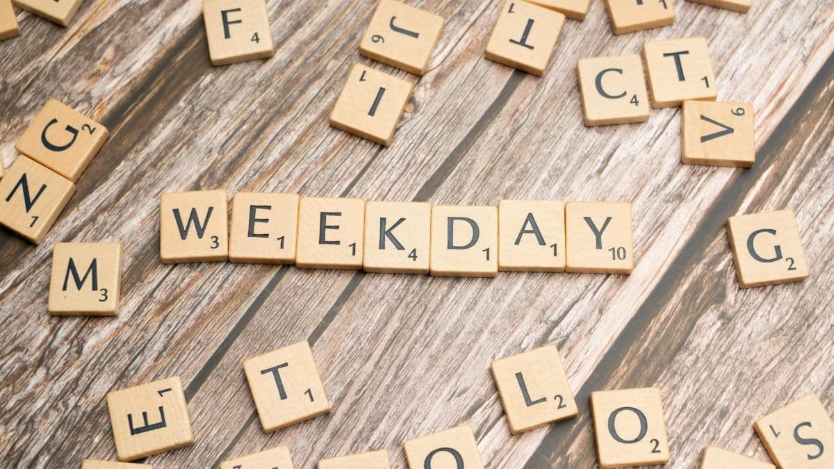 Scattered wooden letter tiles spell 'WEEKDAY' on a rustic wooden surface.
