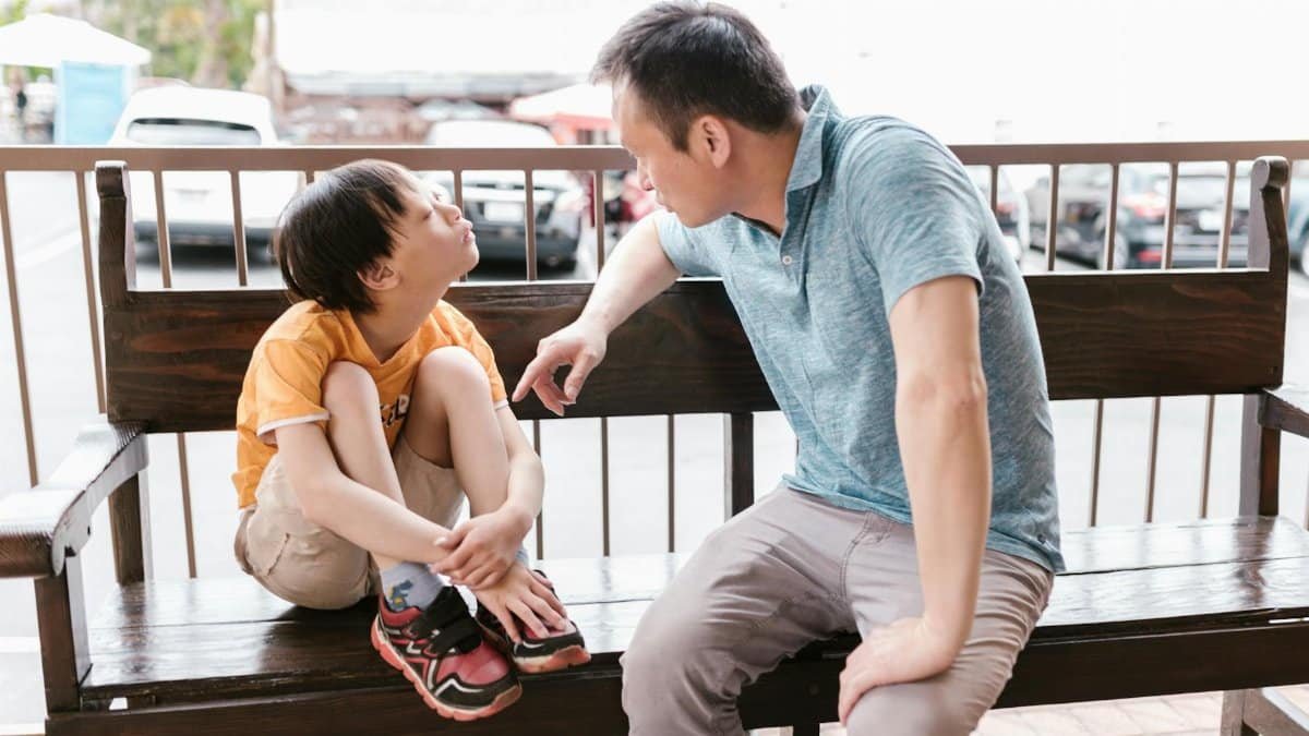 A heartfelt interaction between father and son sitting on a wooden bench outdoors, promoting bonds and autism awareness.