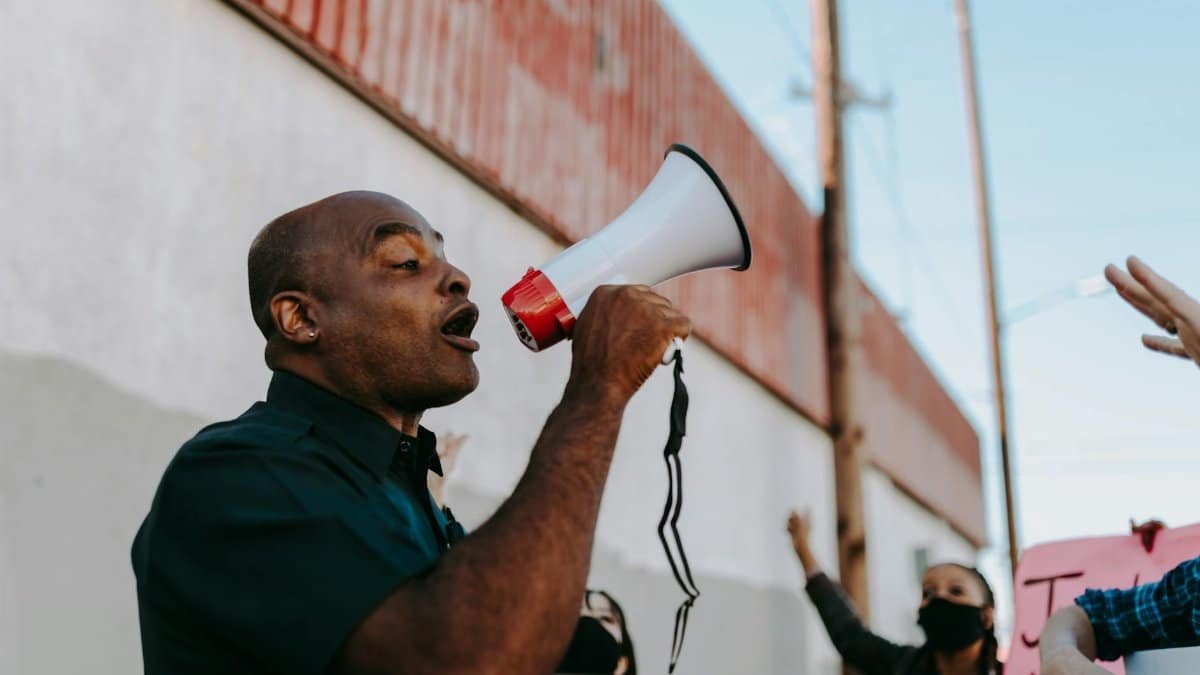 African American man using megaphone to lead a protest outdoors during the day.