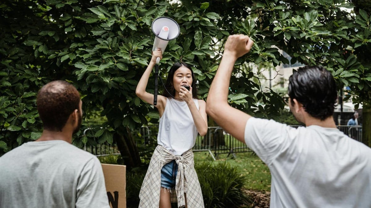 Young activists leading a public protest with a megaphone in a green park setting.