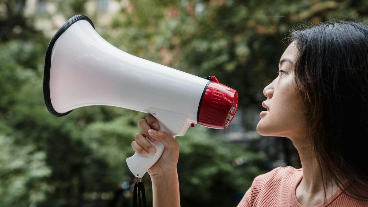 Side view of a young woman holding a megaphone during a protest outdoors.