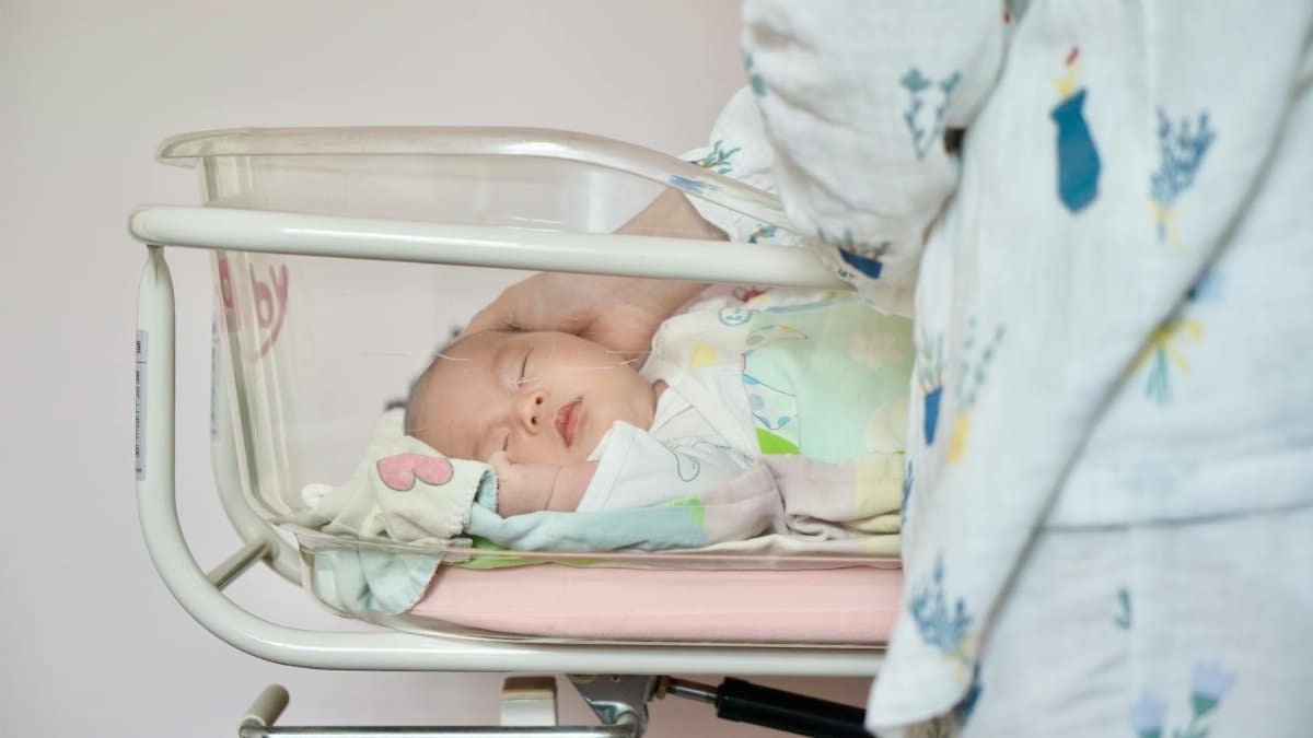 A tender moment of a newborn baby sleeping peacefully in a hospital bassinet being gently touched by a parent.