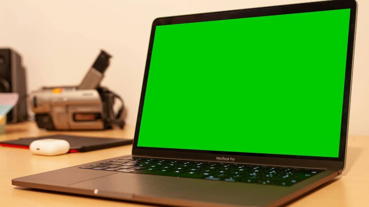 MacBook Pro with green screen on desk, ideal for video editing setups or tech presentations.