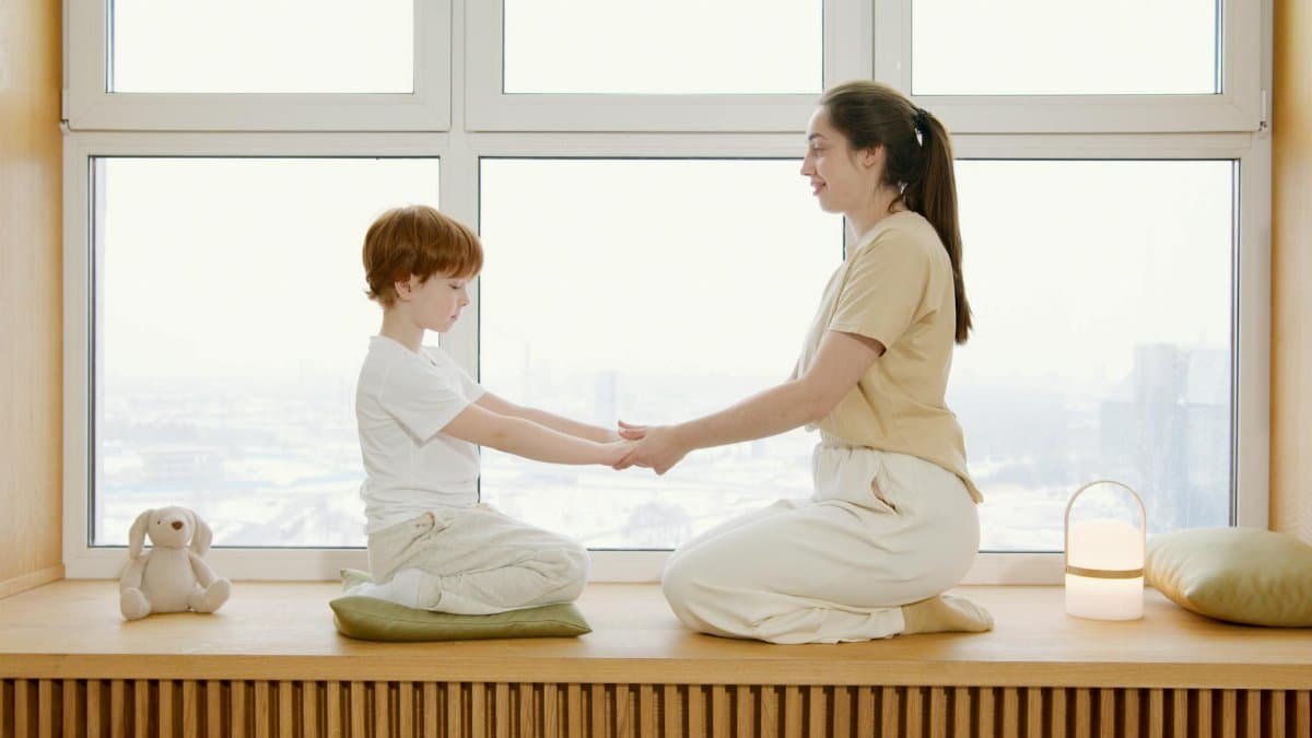 Mother and son practicing mindfulness meditation at home by a large window.