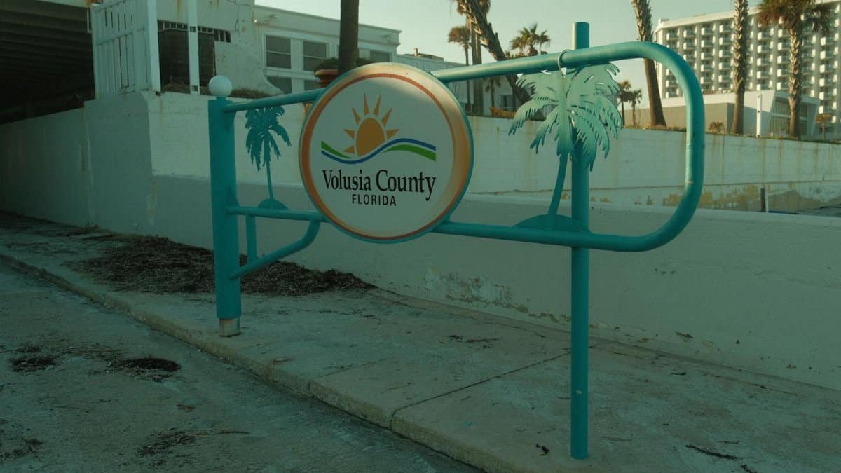Sign at Volusia County, Florida beachfront entrance with palm trees.