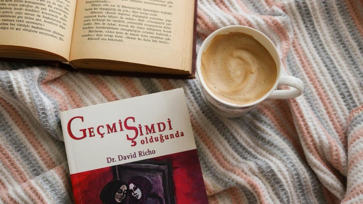 Flat lay of a cozy reading setup with books and a cup of coffee on a striped blanket.