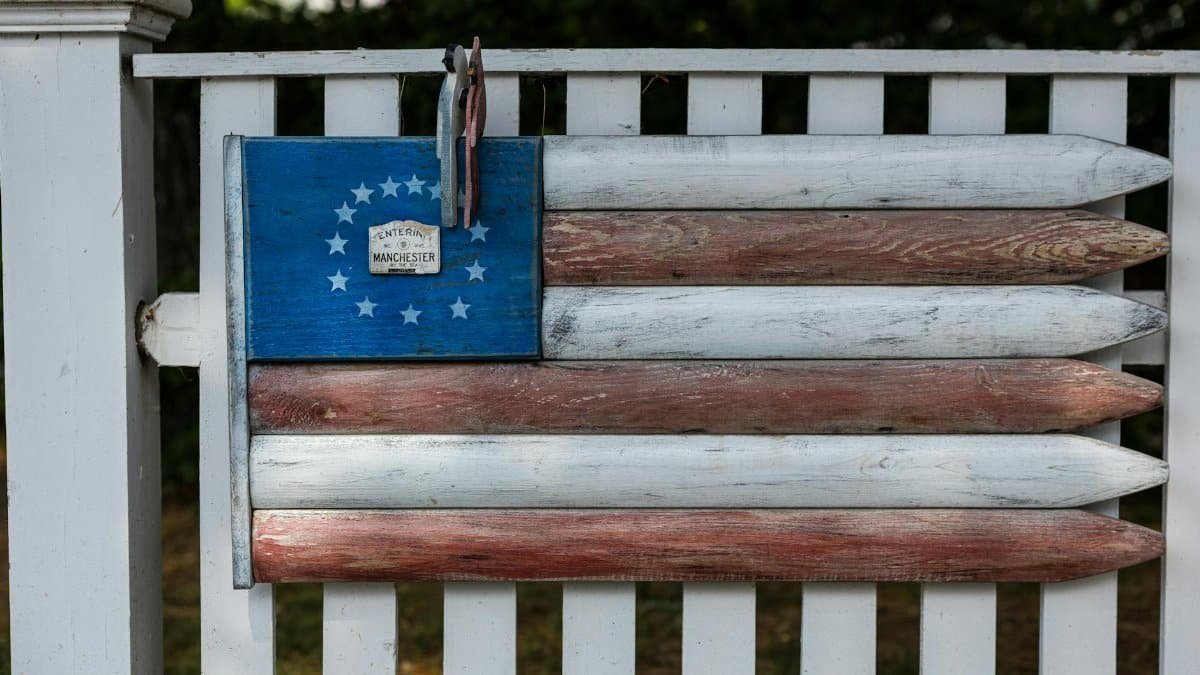 Close-up of a rustic American flag decoration on a wooden fence, symbolizing patriotism.