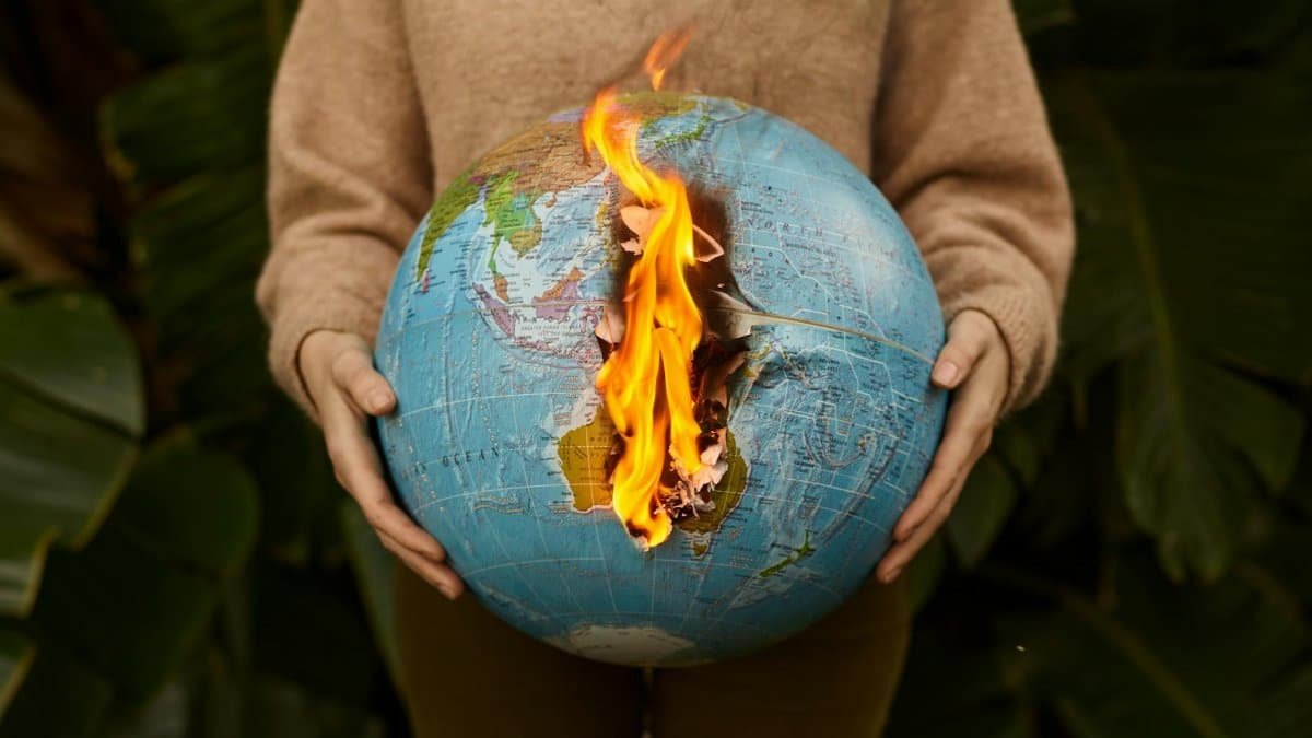 A symbolic portrayal of climate change with a burning globe held in hands, set against a nature background.