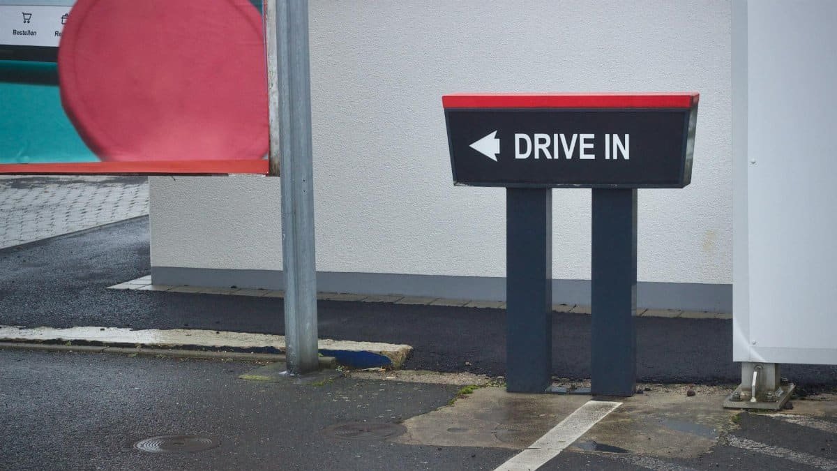 Outdoor drive-in sign at fast food drive-thru entrance on a rainy day.