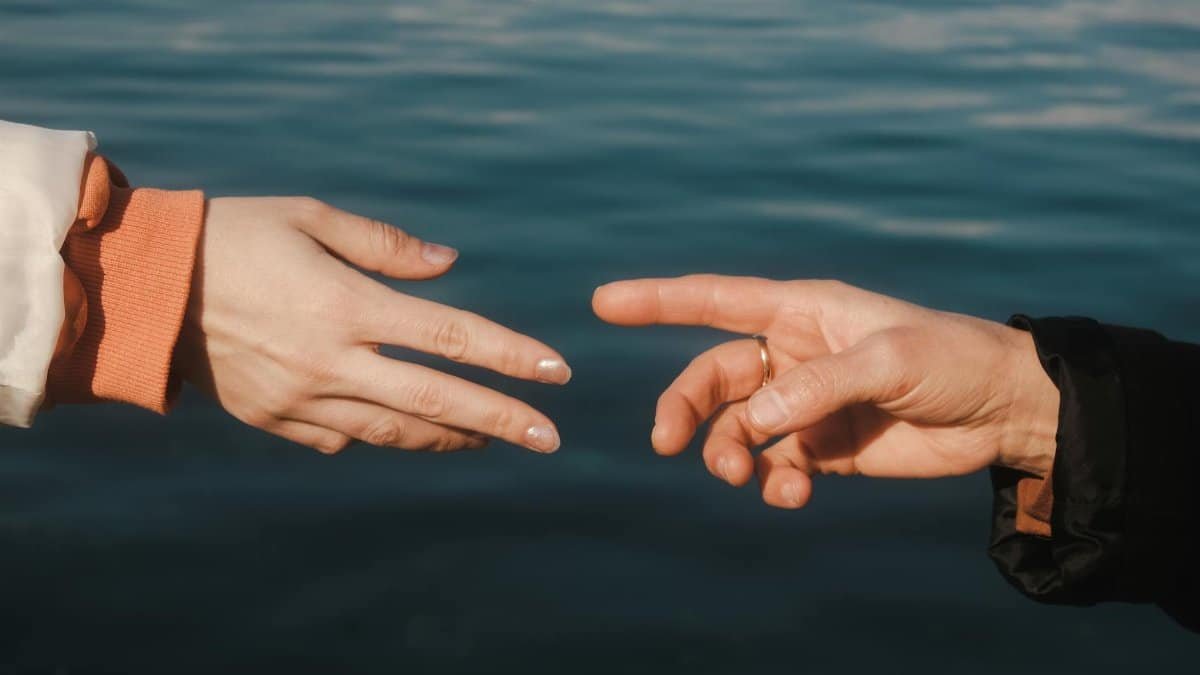 Two hands reaching towards each other over a tranquil blue sea background, creating a sense of connection.