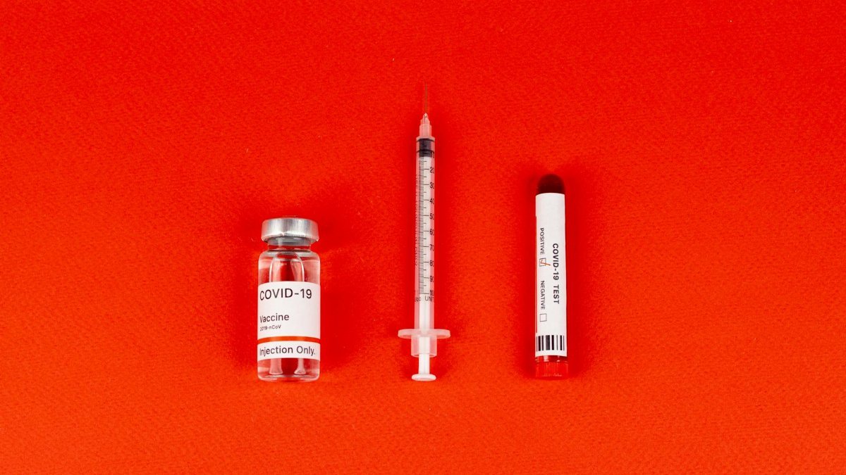 COVID-19 vaccine vial, syringe, and test tube arranged on a red background, symbolizing healthcare.