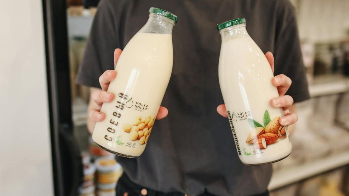 Person holding bottles of almond and soy milk substitutes in a store.