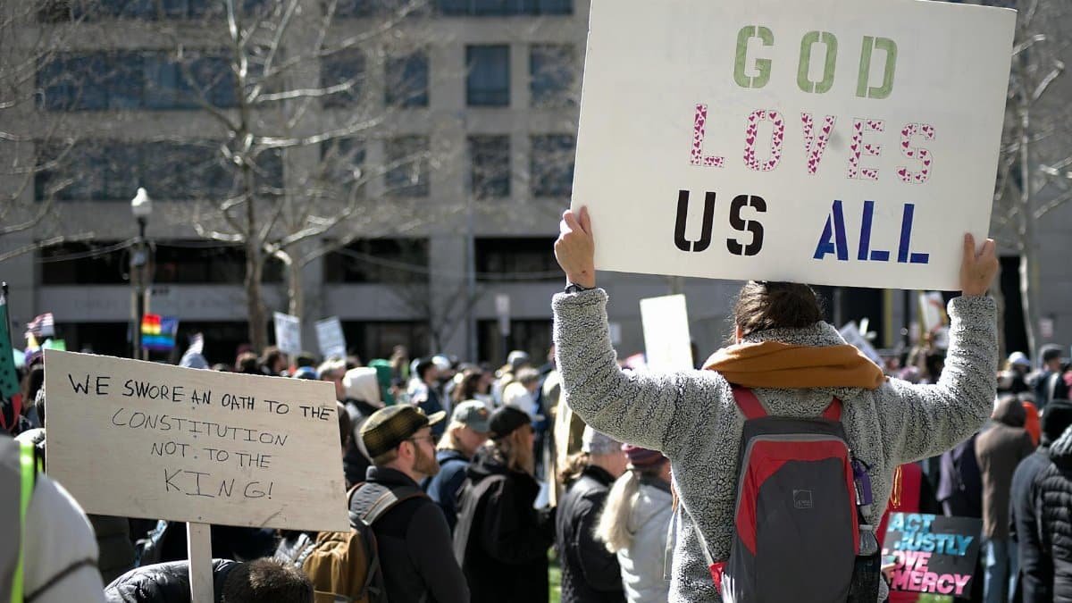 A crowd gathers for a protest in Baltimore holding signs promoting love, equality, and constitutional rights.
