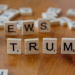 Wooden letter tiles spell 'NEWS' and 'TRUMP' on a wooden table, relating to political discourse.