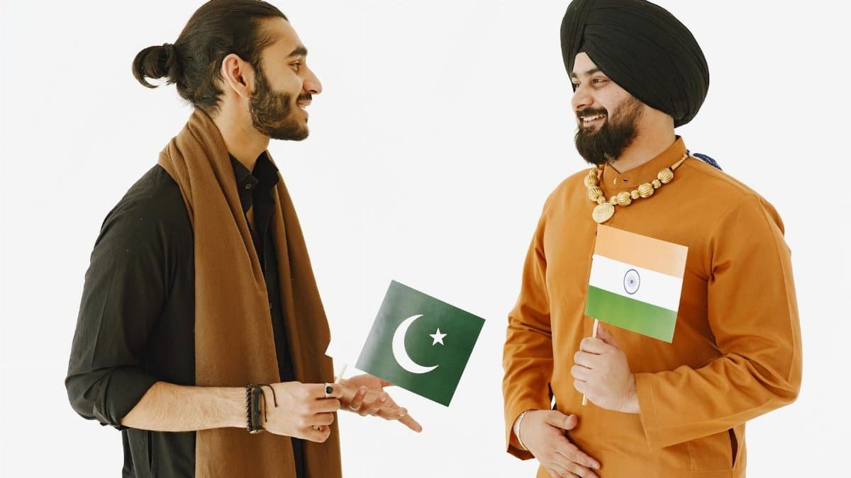 Two men, holding Indian and Pakistani flags, engage in friendly conversation.