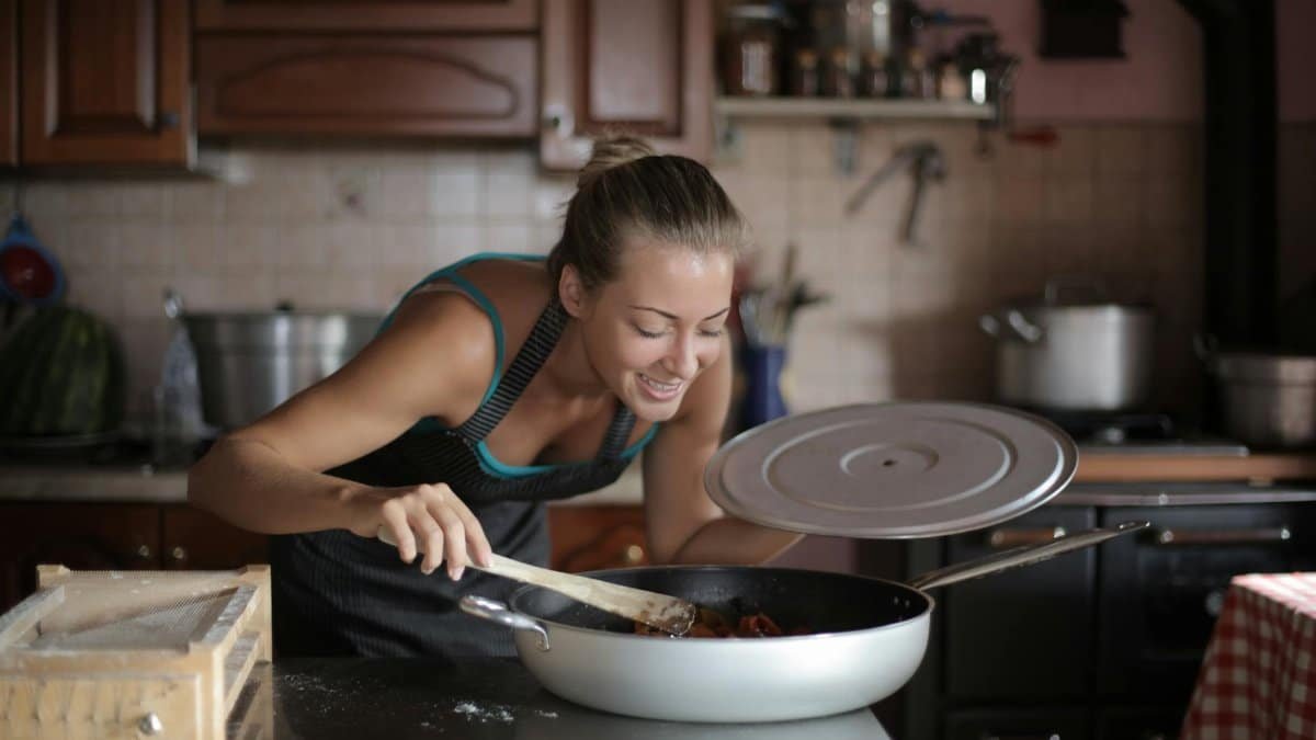 Woman smiling while cooking in a warm kitchen environment, embracing the joy of food preparation.