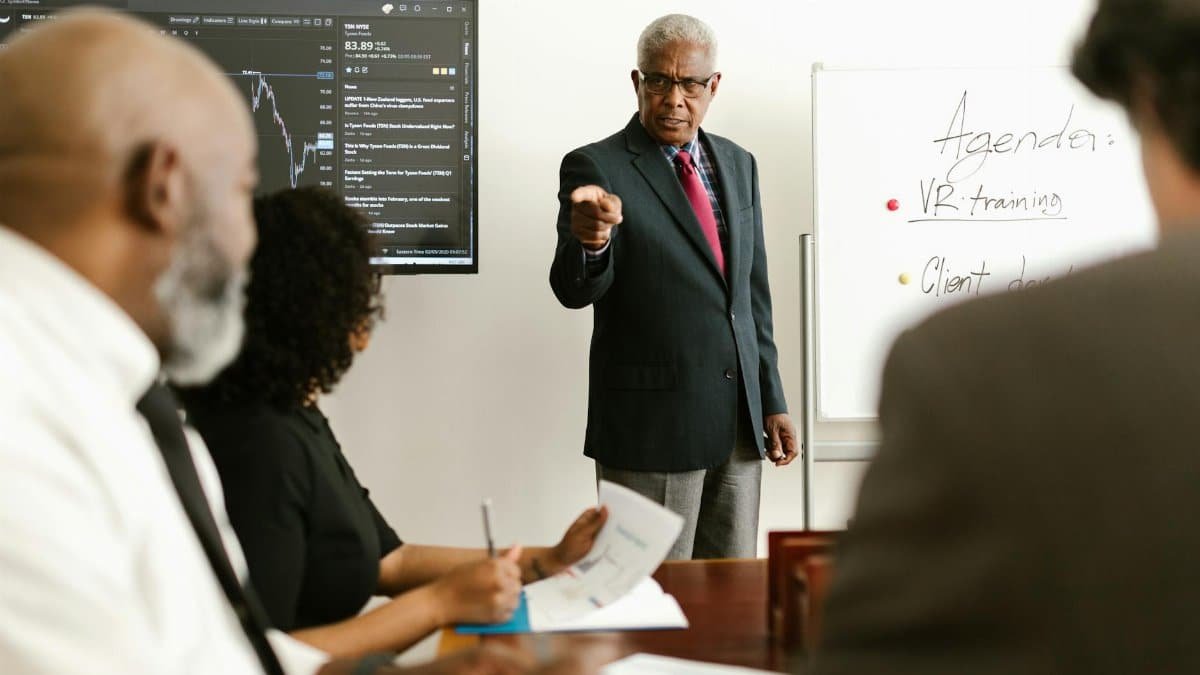 Senior executive conducting a business meeting with colleagues, discussing agenda on a whiteboard.