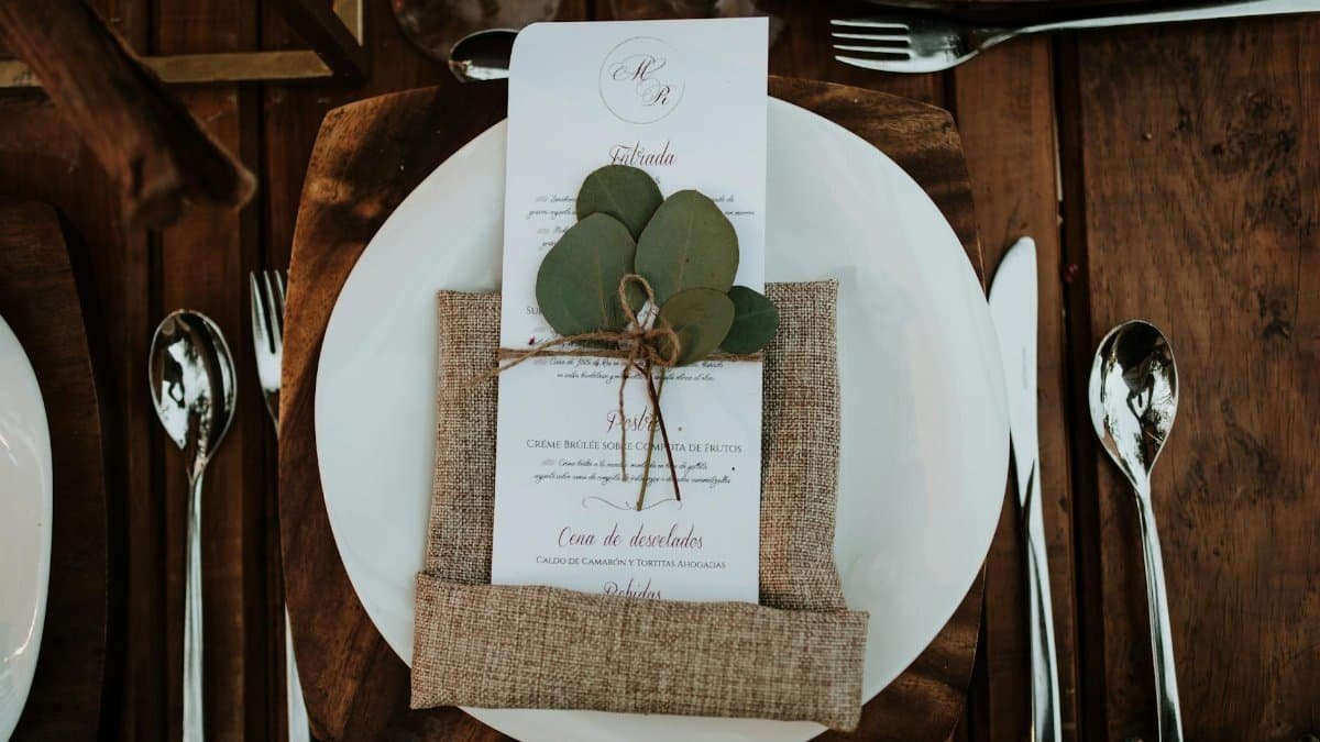 Stylish table setup featuring a menu card with eucalyptus leaves on a rustic wooden table.