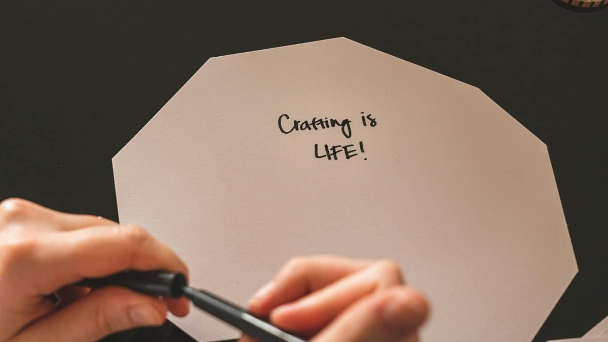 Close-up of hands writing 'Crafting is life!' on paper with marker pen, highlighting creativity.