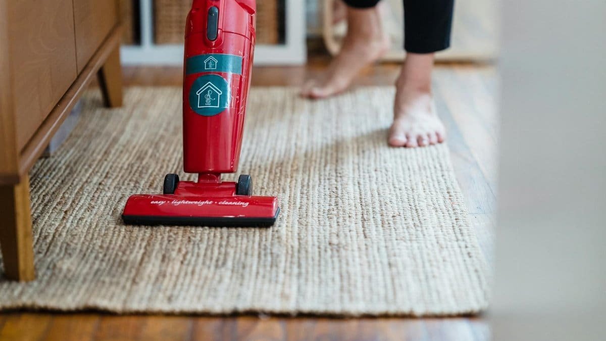 A red vacuum cleaner on a carpet in a stylish home setting with barefoot user.