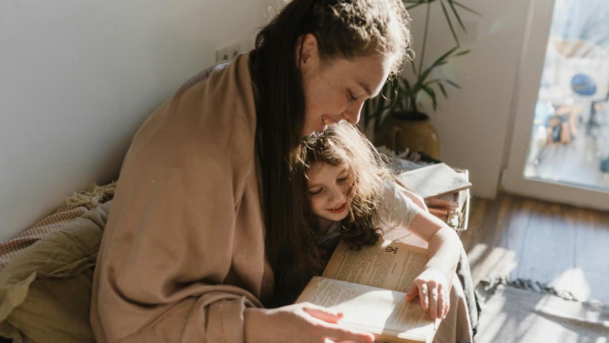 A warm moment of a mother and daughter reading a book by the window.