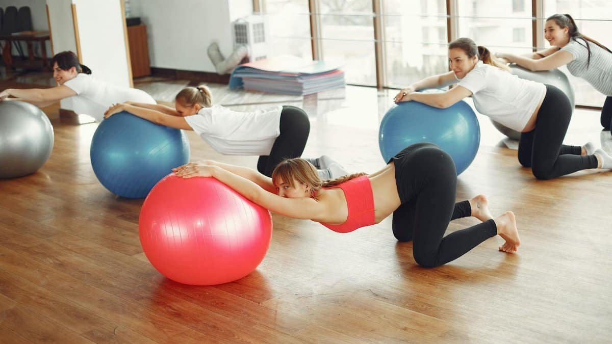 Cheerful young pregnant women wearing sportswear performing exercises together with female fitness instructor during prenatal workout in light modern studio at daytime