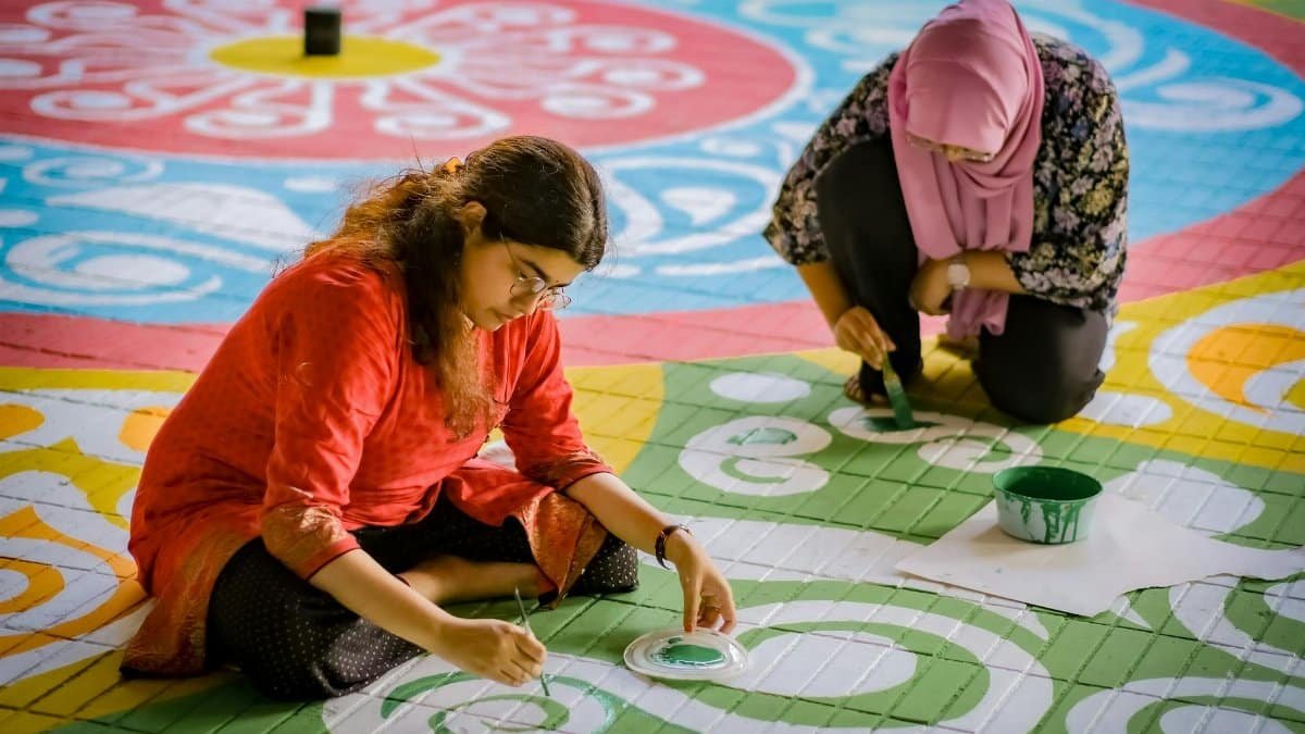 Two women engaged in creating a vibrant and colorful floor art with intricate patterns.