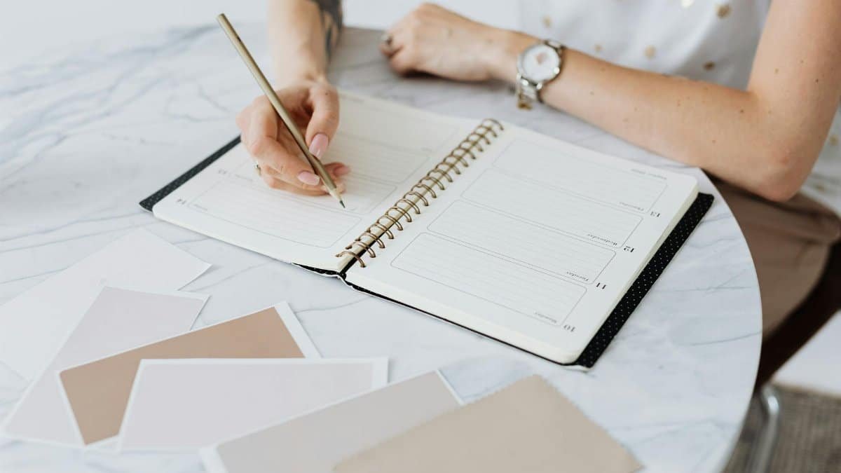 A woman writes in a planner on a marble table, surrounded by swatches. Creative and organized workspace.