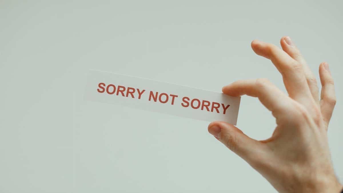 Hand holding a card with the phrase 'Sorry Not Sorry' on a neutral background.