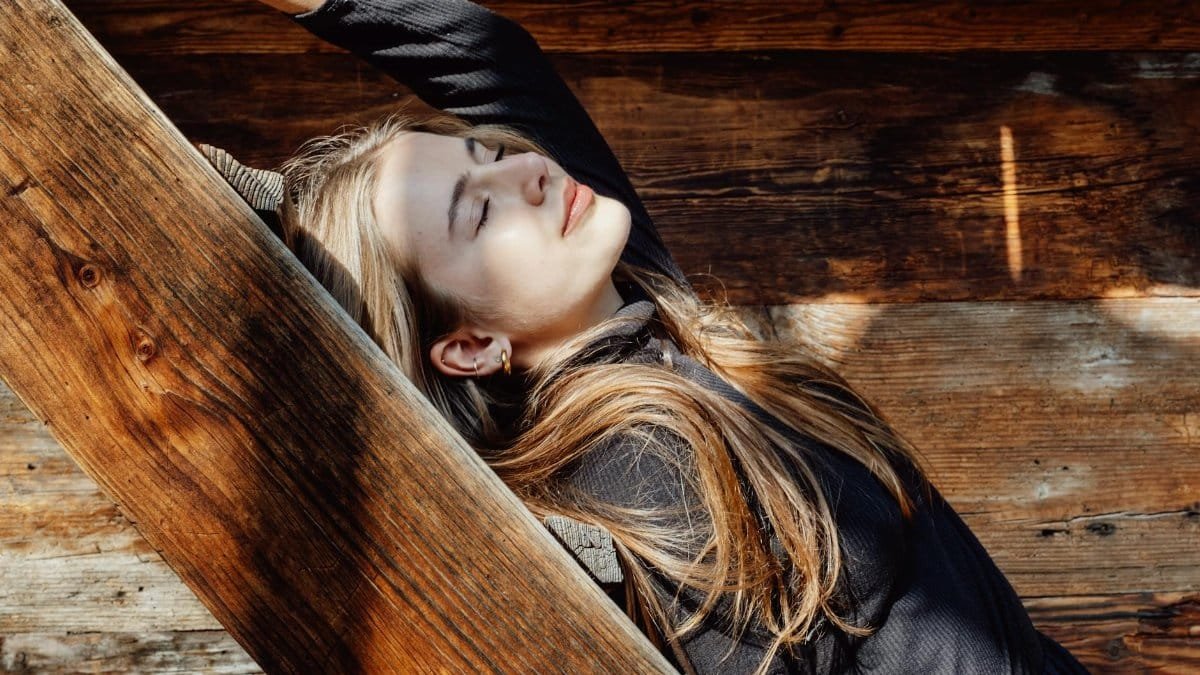 A woman with long hair enjoys sunlight while reclining on wooden stairs.