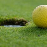 A yellow golf ball close to the hole on a grassy golf course.