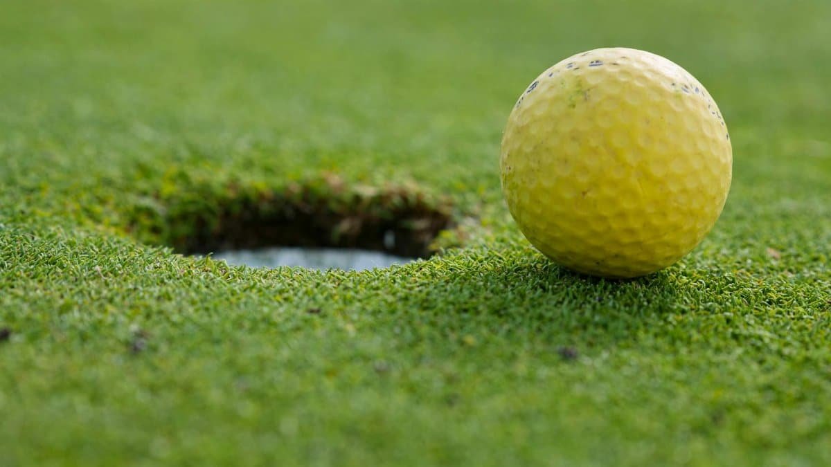 A yellow golf ball close to the hole on a grassy golf course.