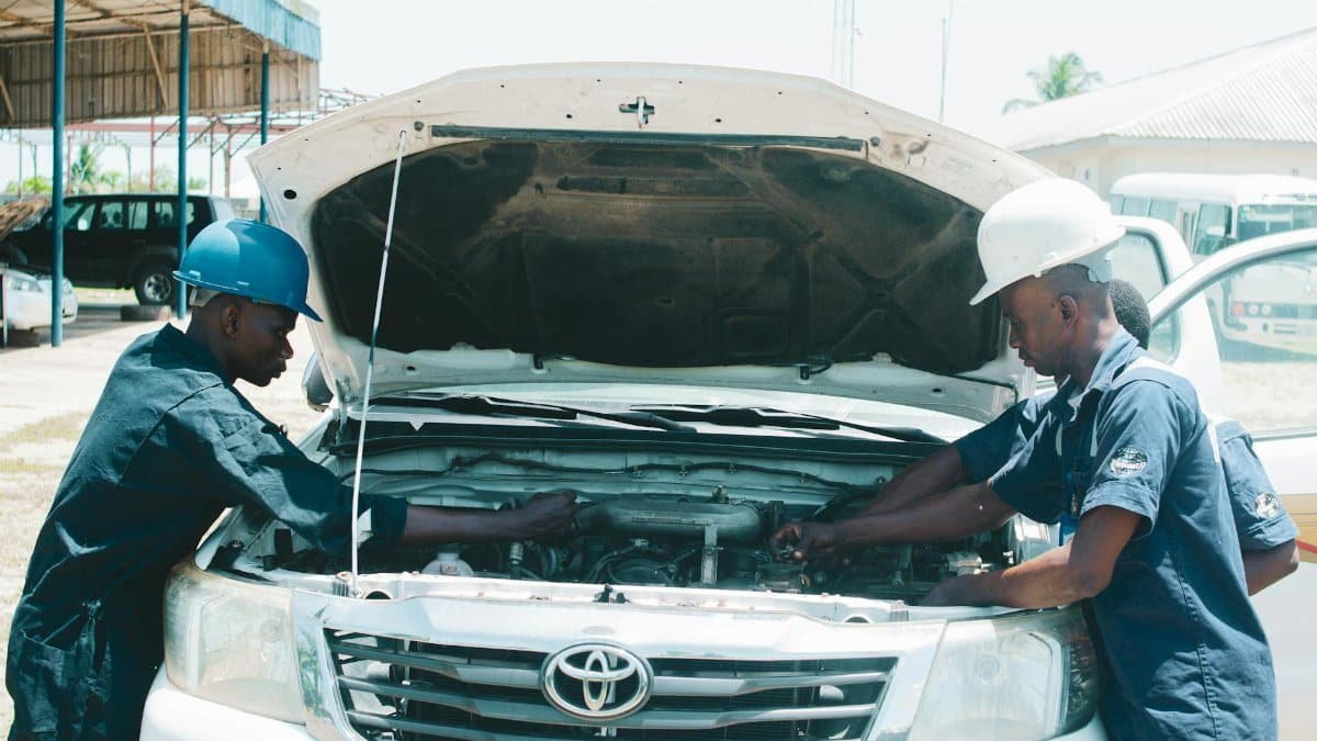 Two African mechanics checking a Toyota engine outdoors in AK, Nigeria, showcasing teamwork and collaboration.