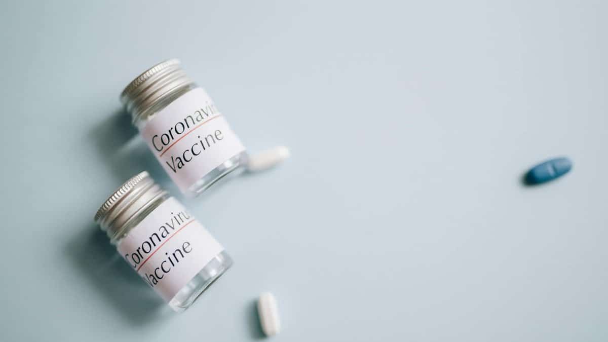 Close-up of coronavirus vaccine vials with scattered pills on a blue background, symbolizing healthcare efforts.