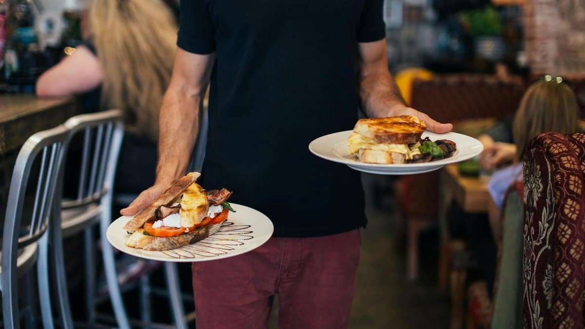 Crop faceless waiter holding plates with appetizing sandwiches in with toasted bread in modern restaurant during lunch