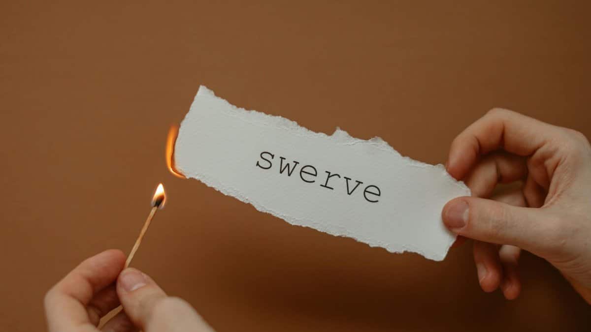 Close-up of hands holding burning paper with 'swerve', symbolizing change or danger.