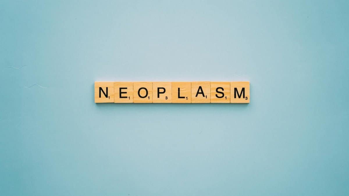Scrabble tiles arranged to spell 'neoplasm' on a blue surface symbolizing cancer awareness.