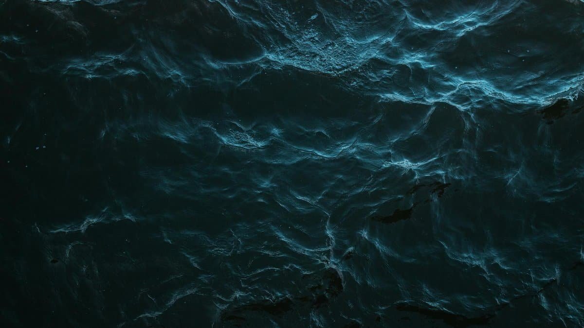 Mysterious dark ocean surface with subtle light reflections and deep blue hues.