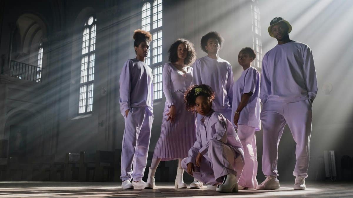 A fashionable group in pastel attire posing dramatically in a sunlit church interior, casting long shadows.