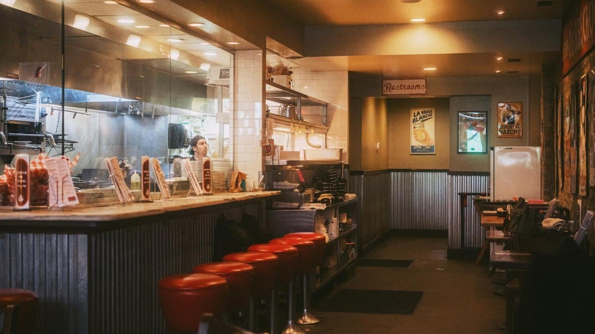 Warm and inviting interior of a classic American diner with red stools and open kitchen.