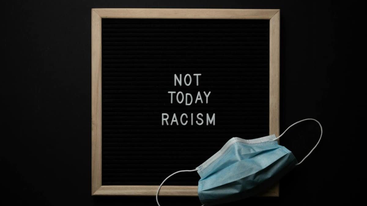 Overhead view of medical mask located on blackboard with white NOT TODAY RACISM inscription on center against black background