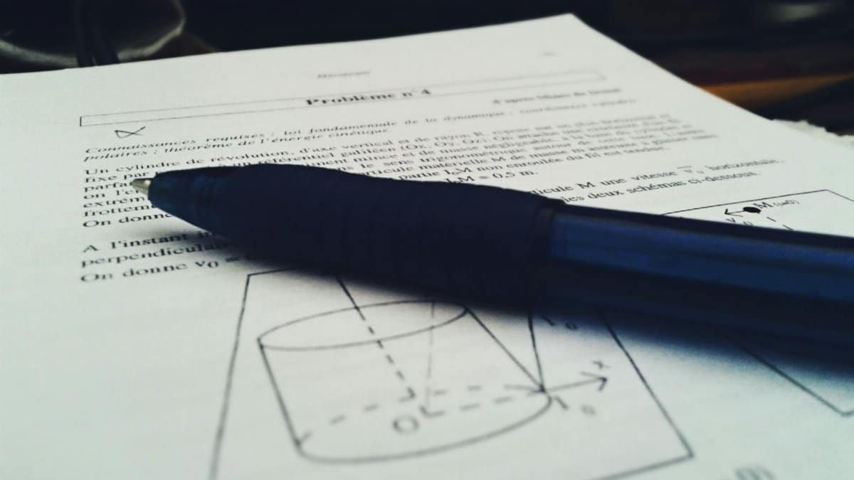 Close-up shot of a physics document with a blue pen on top, focused on equations.
