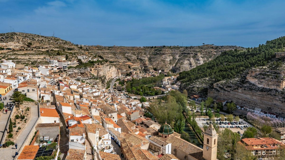 Aerial view of historic Alcalá del Júcar with rugged cliffs and lush greenery in spring.