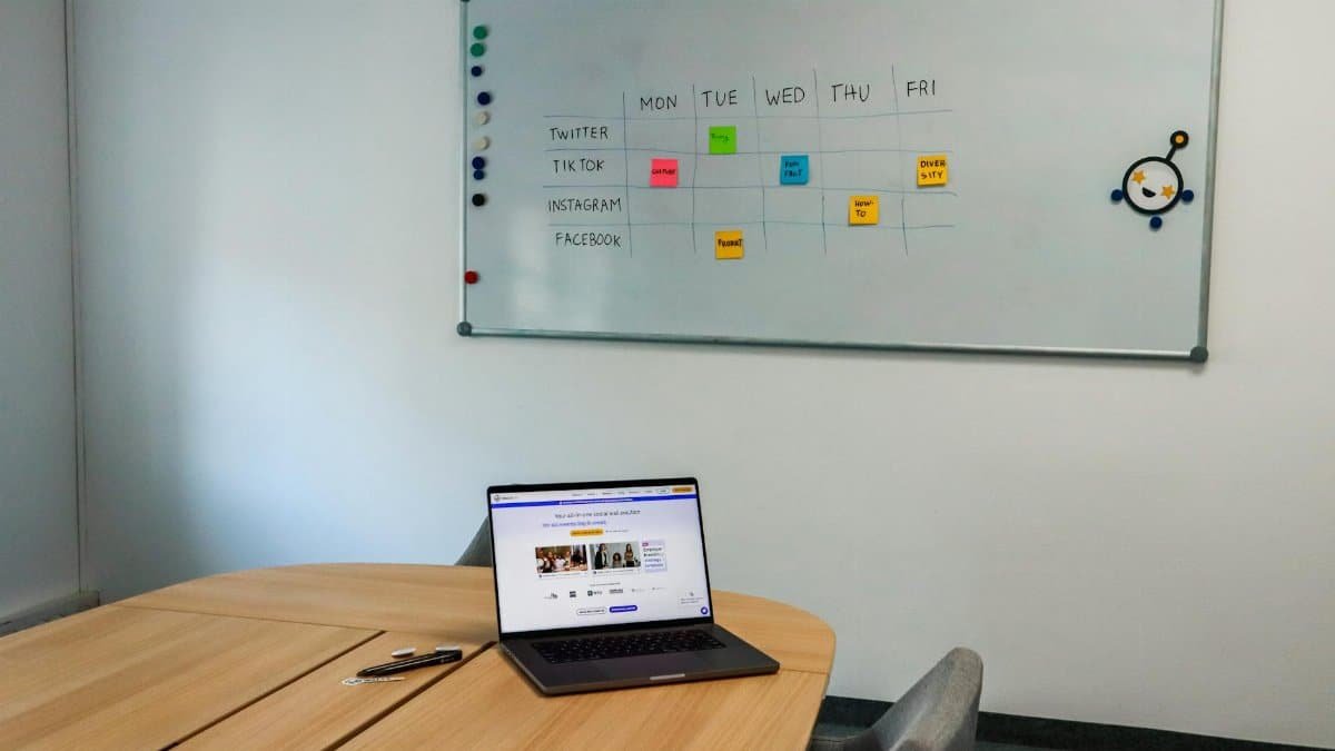 Office setup featuring a conference table, laptop, and organized whiteboard schedule, highlighting a tech-driven workspace.
